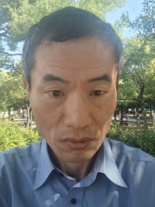 石倉裕三の顔写真。緑の公園で、セミナーの内容を考えている様子